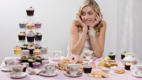 Frau an einem Tisch, umgeben von Cupcakes und anderen Desserts